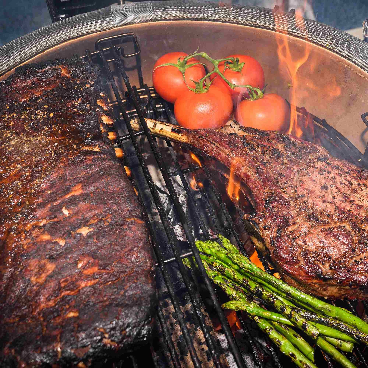 Grilled steak, tomatoes, and asparagus on a barbecue grill with flames.